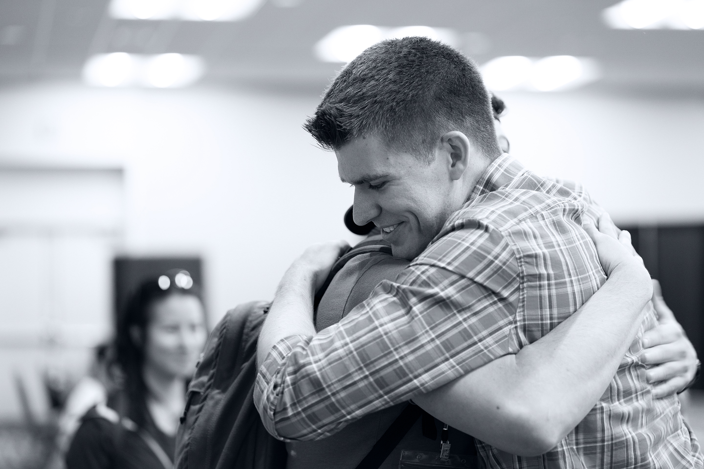 Young man in plaid shirt giving a hug to a person with a backpack